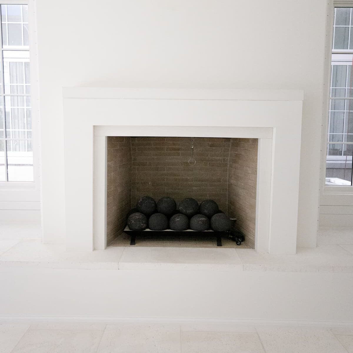 0S1A5598precast A modern, white fireplace with black decorative stone spheres inside, set against a neutral wall with windows on either side.