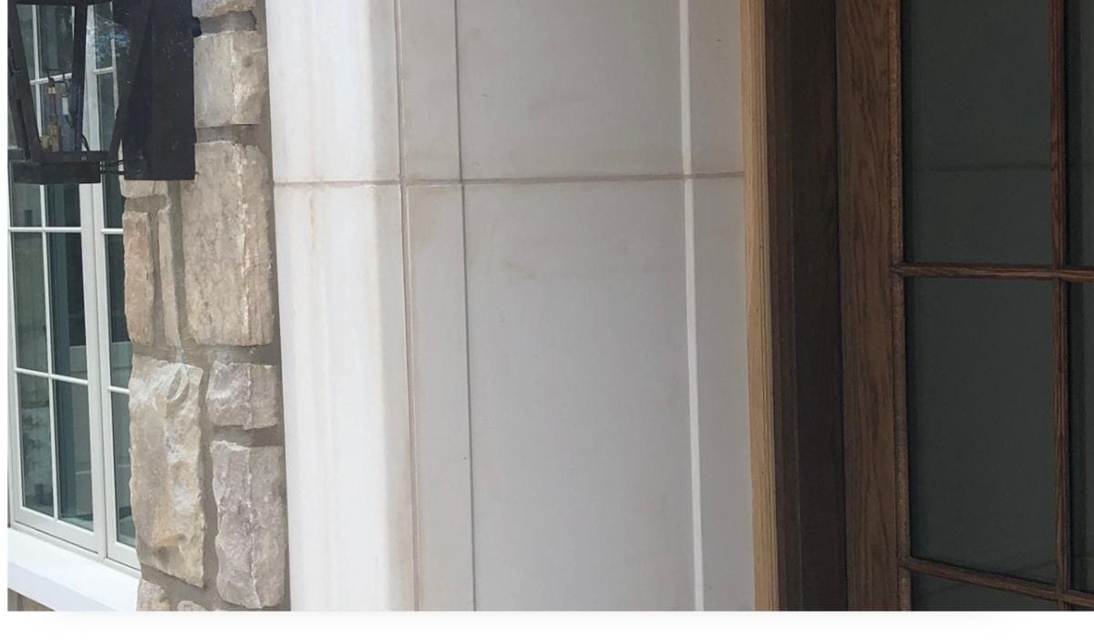 Door Casing Close-up of a house exterior showing a stone wall, a window with white concrete casing, a mounted black lantern, and part of a wooden door with glass panels.
