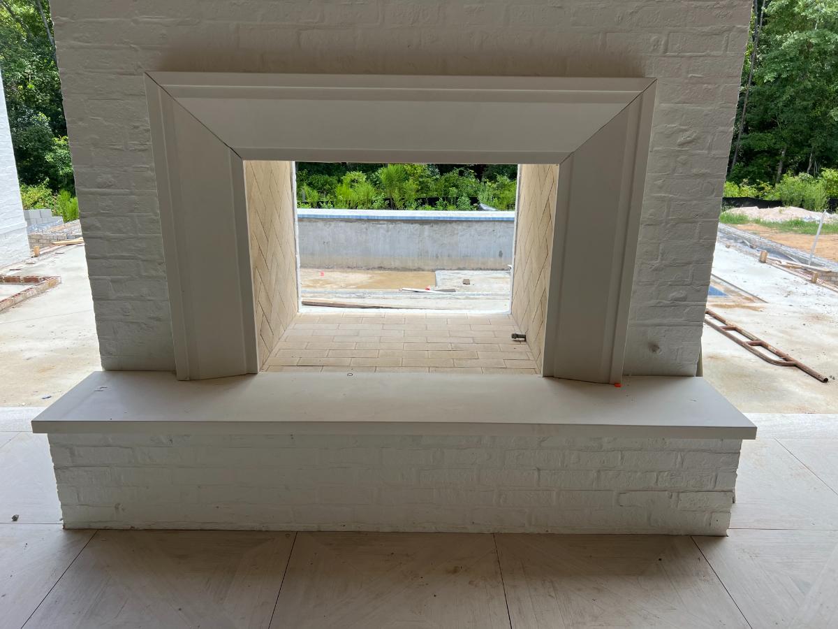 Exterior Surround and Hearth A rectangular white brick outdoor fireplace with a precast surround, showing a view of greenery outside.