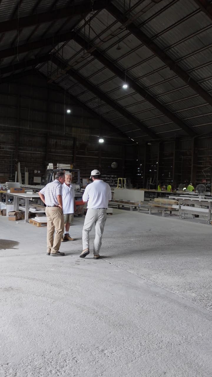 plant 2 The Riviera Stoneworks management team stand and talk inside a large industrial warehouse, with tables, equipment, and more workers visible in the background.
